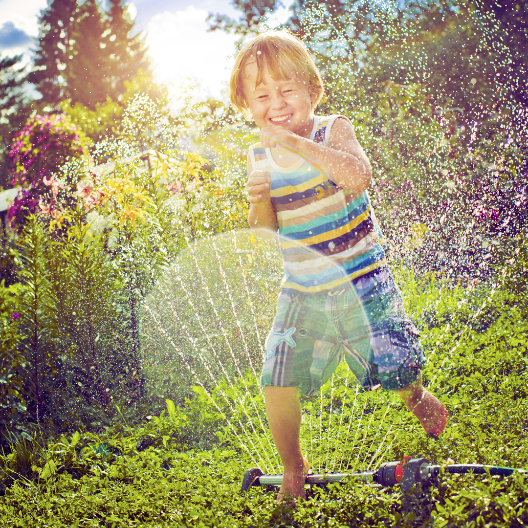 A young child plays in a sprinkler.