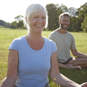 A smiling mature woman practices yoga outside.